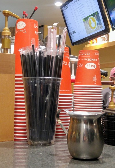 Image taken in a coffee shop of plastic-wrapped straws and take-out cups.